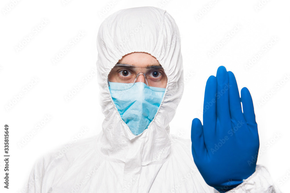 Portrait of young man in protective white medical uniform giving STOP sign during coronavirus pandemic. Epidemic, pandemic of coronavirus covid 19. Portrait of young man in protective white medical uniform giving STOP sign during coronavirus pandemic. Epidemic, pandemic of coronavirus covid 19.