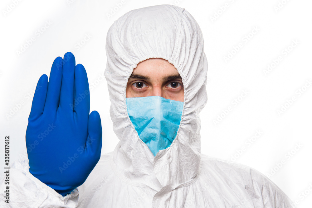 Portrait of young man in protective white medical uniform giving STOP sign during coronavirus pandemic. Epidemic, pandemic of coronavirus covid 19. Portrait of young man in protective white medical uniform giving STOP sign during coronavirus pandemic. Epidemic, pandemic of coronavirus covid 19.