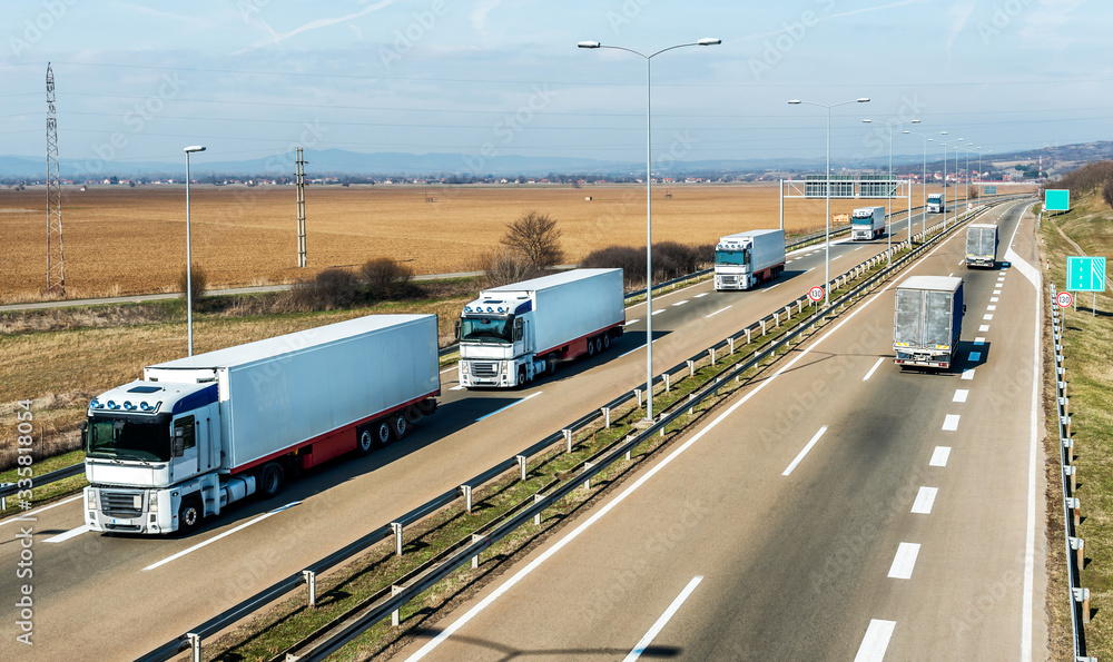 Convoy of White transportation  trucks in line as a caravan or convoy on a countryside highway under a blue sky