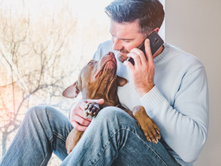 Handsome man and a charming puppy. Close-up, indoors. Studio photo, white color. Concept of care, education, obedience training and raising pets