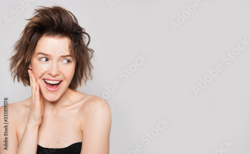 Shocked and surprised girl smiling and looking to the side presenting your product isolated grey background. Natural beauty no make up woman amazed. Free space for text. Expressive facial expressions