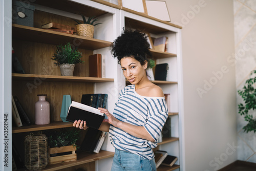 Ethnic woman with open book nearby bookshelves