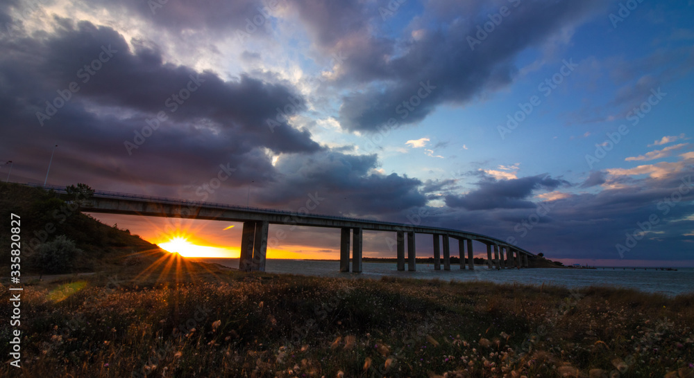 Sunset under the bridge to Noirmoutier, France, with frozen fast-moving clouds