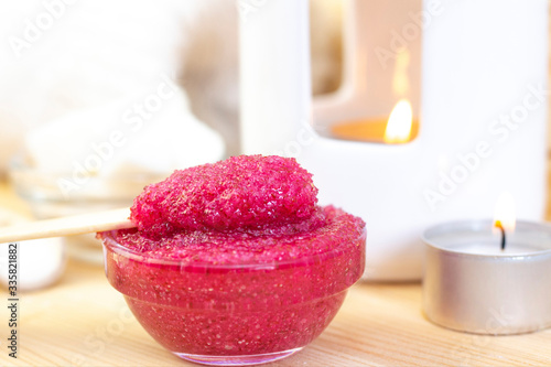 Natural pink body scrub made from sugar. Pink scrub in a glass cup on a background of candles and sugar.