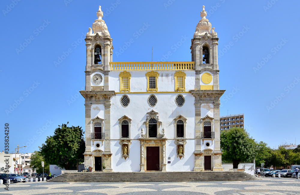 Faro / Algarve, Portugal - Church of Carmo, a white building with yellow décor, steps in front of the church and paving slabs of Calzada Portuguese, blue sky, in the summer during the daytime. 