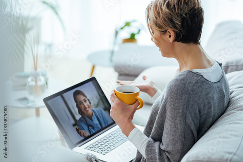 Foto Woman using laptop and having video call with her doctor while sitting at home