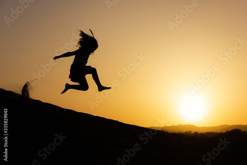 Little girl jumping over sand dunes on sunset in Maspalomas, Gran Canaria. Brave kid silhouette in the air at twilight in Canary Islands, Spain. No fear, courage, dare concepts