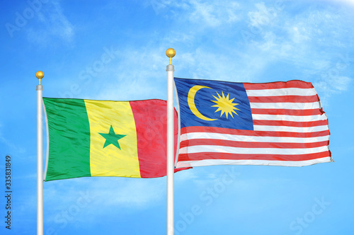 Senegal and Malaysia two flags on flagpoles and blue cloudy sky