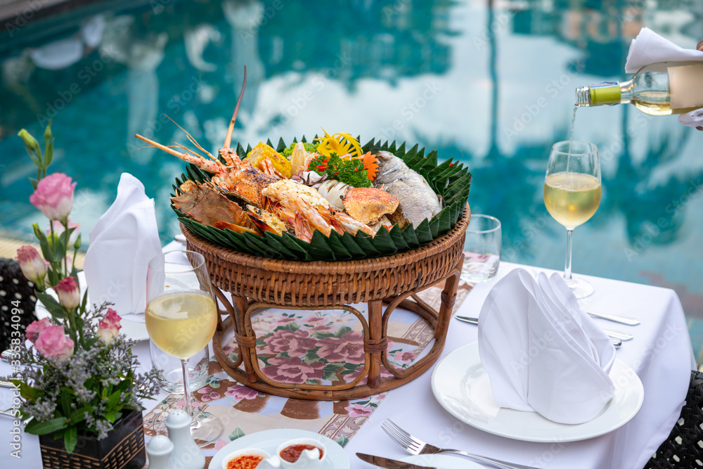 Luxury romantic seafood dinner set up by the pool for couple with glasss of white wine.