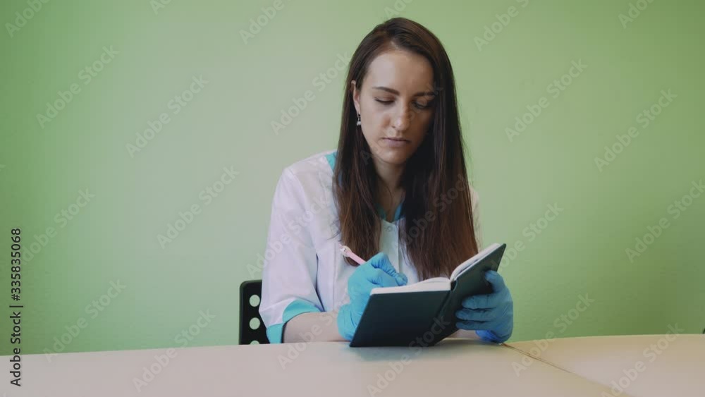 Doctor is writing something in her notebook while spending time indoors in her cabinet. Doctor is writing something in her notebook while spending time indoors in her cabinet.