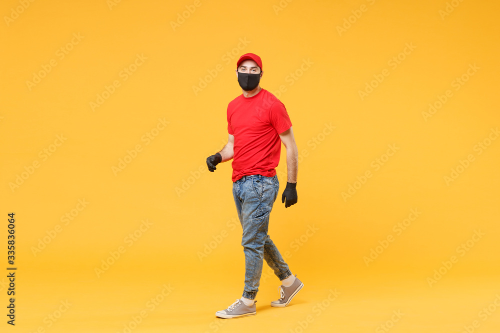 Full length delivery man in red cap t-shirt uniform sterile face mask gloves isolated on yellow background studio Guy employee courier Service quarantine pandemic coronavirus virus 2019-ncov concept. Full length delivery man in red cap t-shirt uniform sterile face mask gloves isolated on yellow background studio Guy employee courier Service quarantine pandemic coronavirus virus 2019-ncov concept.