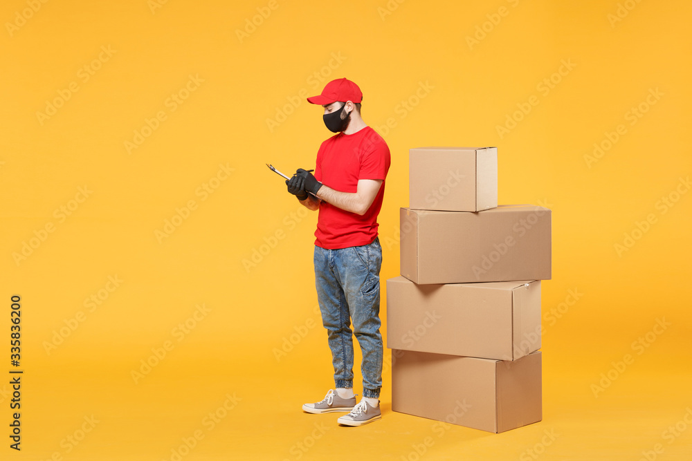 Delivery man employee in red cap blank t-shirt uniform face mask glove hold empty cardboard box isolated on yellow background studio Service quarantine pandemic coronavirus flu virus 2019-ncov concept Delivery man employee in red cap blank t-shirt uniform face mask glove hold empty cardboard box isolated on yellow background studio Service quarantine pandemic coronavirus flu virus 2019-ncov concept