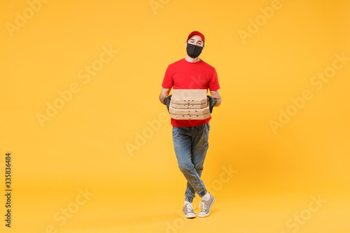 Delivery man employee in red cap t-shirt uniform black mask gloves give food order pizza boxes isolated on yellow background studio. Service quarantine pandemic coronavirus virus flu 2019-ncov concept