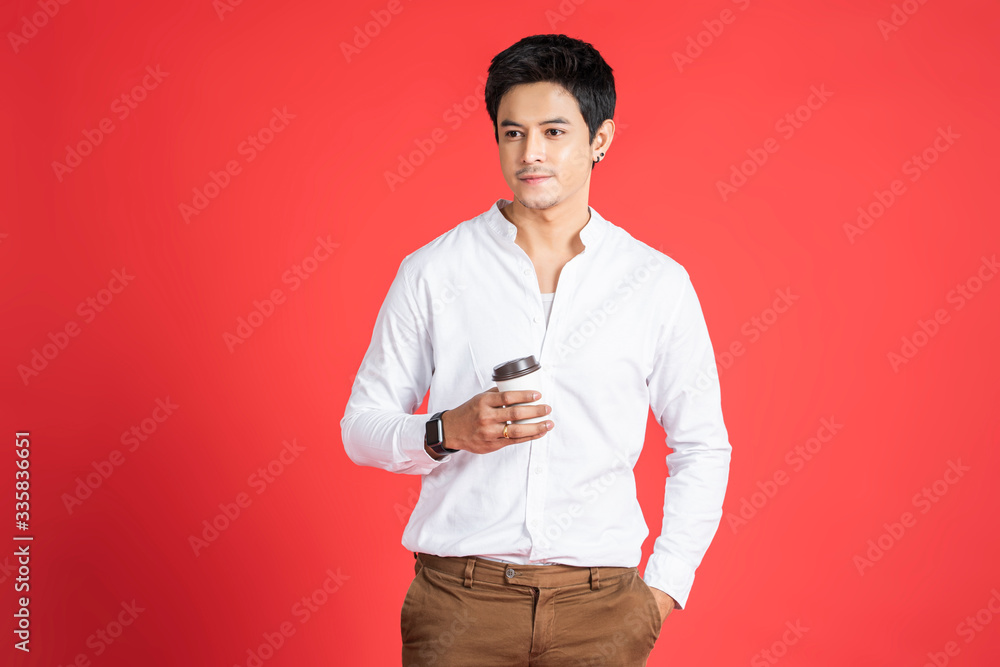 handsome asian businessman smiling holding a plastic cup of coffee from cafe store taking a break time from hard work, hand in pocket wearing casual clothing standing posing in red isolated background handsome asian businessman smiling holding a plastic cup of coffee from cafe store taking a break time from hard work, hand in pocket wearing casual clothing standing posing in red isolated background