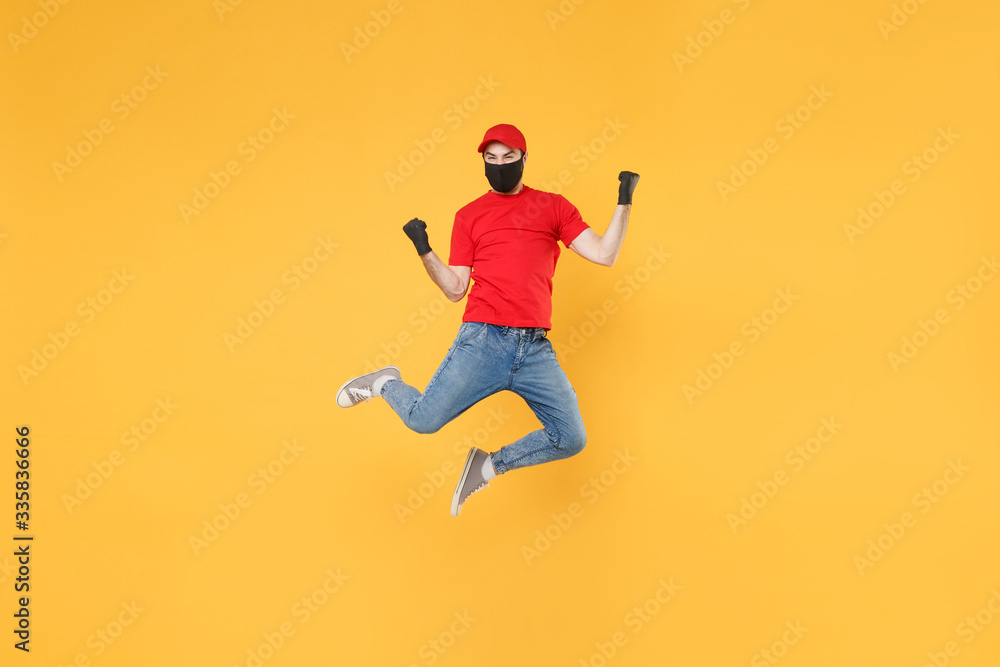 Fun jumping delivery man in red cap t-shirt uniform sterile face mask gloves isolated on yellow background studio Guy employee courier Service quarantine pandemic coronavirus virus 2019-ncov concept. Fun jumping delivery man in red cap t-shirt uniform sterile face mask gloves isolated on yellow background studio Guy employee courier Service quarantine pandemic coronavirus virus 2019-ncov concept.