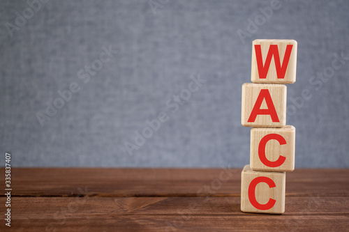 Abbreviation WACC (Weighted Average Cost Of Capital) text acronym on wooden cubes on dark wooden backround. Business concept.