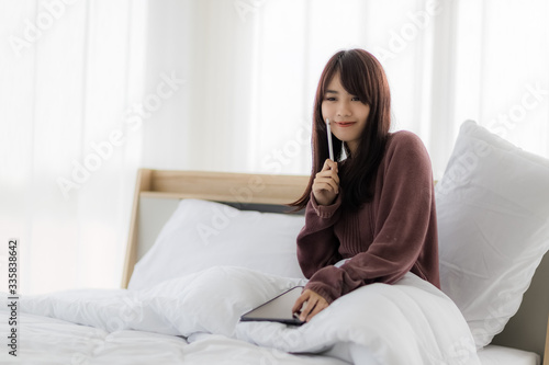 Asian woman using tablet for working, educational, e-commerce, social media in her bed. corovavirus covid-19, stay at home, work form home concept.