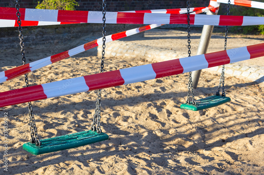 View of a closed playground. The swing is closed with a barrier tape. In the corona crisis there are numerous contact barriers.