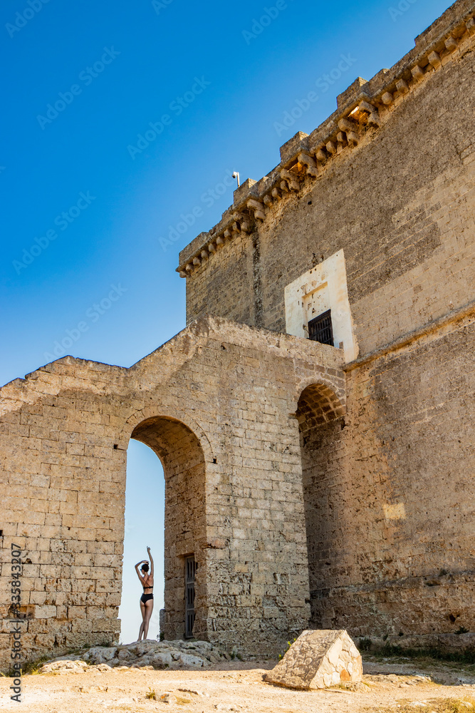 Nardò, Italy, Puglia, Salento. Torre dell'Alto, the watchtower of Porto Selvaggio. A beautiful girl in a black bikini, shot from behind, poses for the photo, under the arch of the staircase. Blue sky.