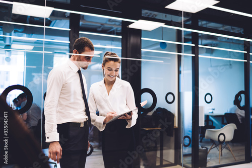 Fototapeta Naklejka Na Ścianę i Meble -  Successful formally dressed woman holding digital tablet for discussing web marketing plan with male employee, cheerful confident colleagues collaborating on business idea standing in office hall