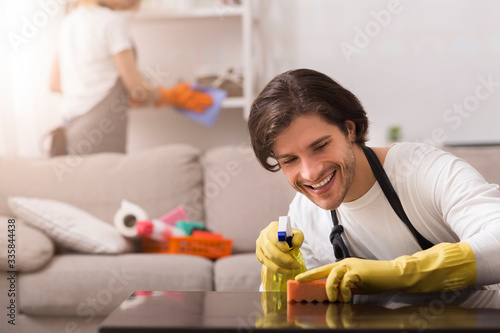 Household Duties. Couple Spring-Cleaning Apartment Together, Man Wiping Dust From Table