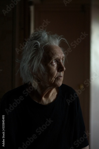 Portrait of grandmother at the home. Grandma sits in the dark and looks at the light.