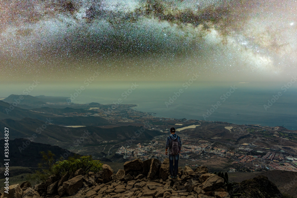 Obraz premium Traveler stays on top of mountain and enjoys the milky way view after sunset. Young tourist stand on the hill with colorful night sky on background. High ISO long exposure shot hight sky concept