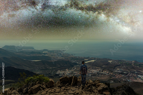 Traveler stays on top of mountain and enjoys the milky way view after sunset. Young tourist stand on the hill with colorful night sky on background. High ISO long exposure shot hight sky concept