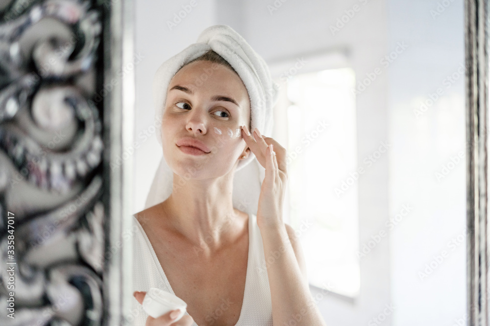 Young adult woman standing in white bathroom with towel on head Young adult woman standing in white bathroom with towel on head