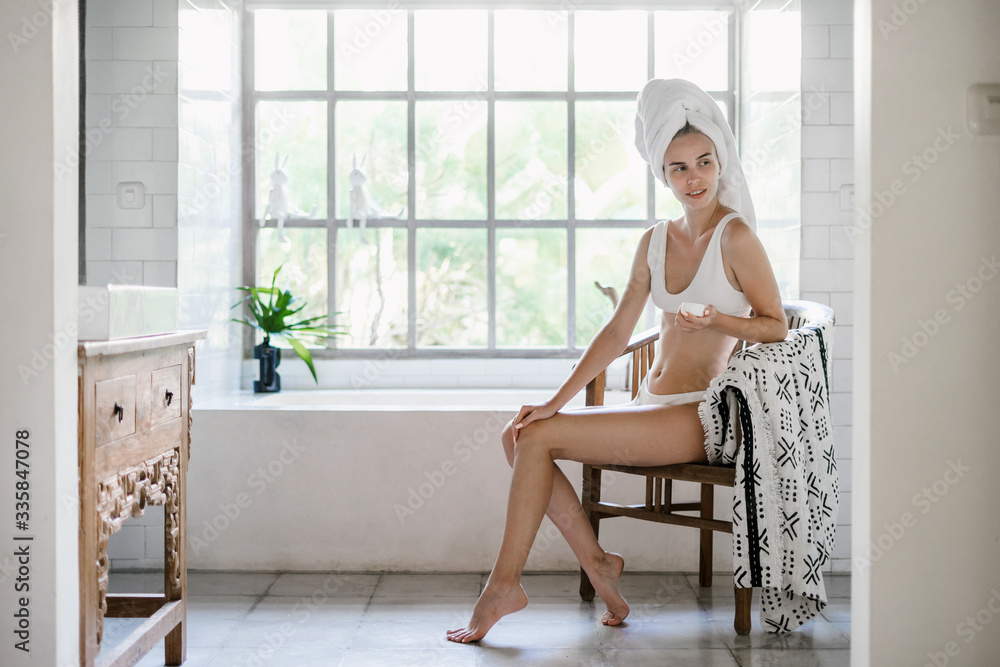 Young adult woman sitting on chair in white bathroom Young adult woman sitting on chair in white bathroom