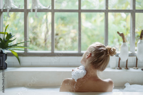 Obraz na płótnie Young adult woman taking bath holding sponge in hand, washed shoulder