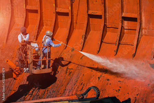 Washing and cleaning, worker High pressure water jet to cleaning with Old ship washing wearing safety harness with in side cargo hold under ship repair in floating dry dock in shipyard