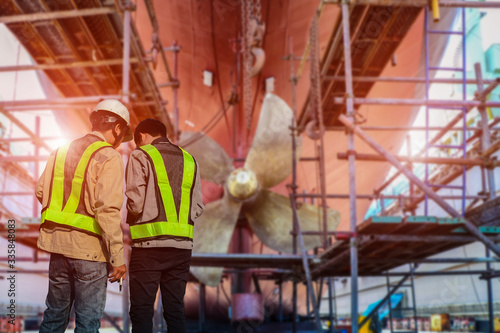 Engineer, surveyor at stern and ship propeller, rudder red after maintenance already by in floating dry dock in shipyard Thailand
