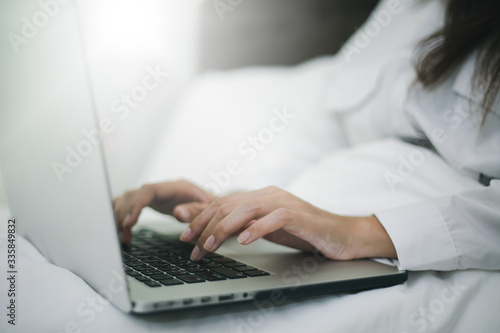 Asian woman using a notebook to work on the bed.She smiles and enjoys working at home.