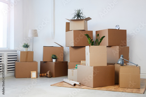 Minimal background image of cardboard boxes stacked in empty room with plants and personal belongings inside, moving or relocation concept, copy space