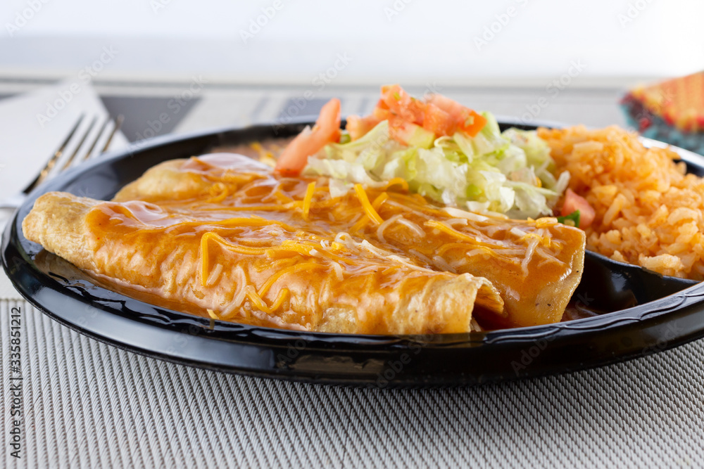 A view of a plate of two enchiladas with a side of rice, in a restaurant or kitchen setting. A view of a plate of two enchiladas with a side of rice, in a restaurant or kitchen setting.