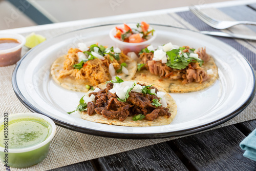A view of three Mexican street tacos on a plate, in a restaurant or kitchen setting.