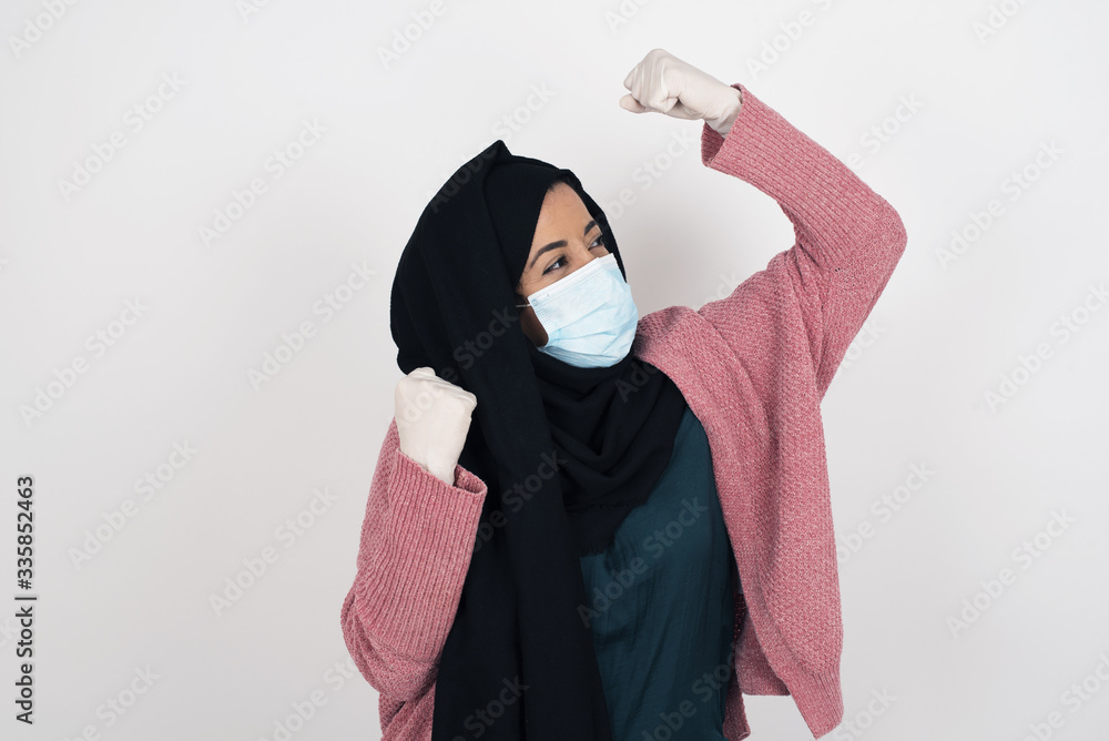 Attractive young muslim woman celebrating a victory punching the air with her fists and a beaming toothy smile over a white studio background with copy space. Attractive young muslim woman celebrating a victory punching the air with her fists and a beaming toothy smile over a white studio background with copy space.