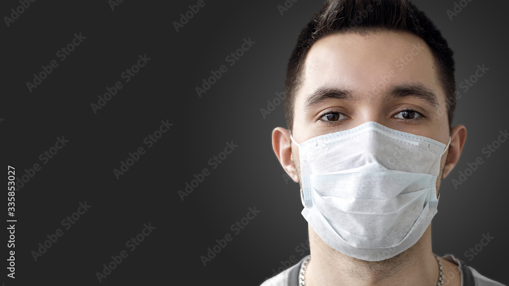 A person wears a protective mask to prevent the spread of airborne coronavirus infection 2019-nCov. Studio photo, banner, on a dark background.