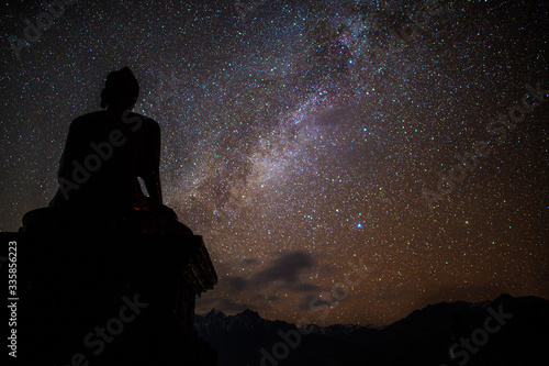 Buddha in meditation beneath starry sky at night with Milky Way galaxy