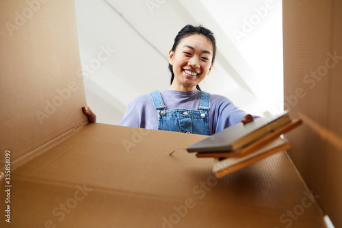 Fotografie Low angle view at young Asian woman looking into cardboard box and smiling happi