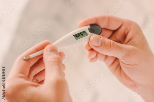 Closeup doctor looking at electronic thermometer with high fever body temperature in hospital. Sick man patient holding digital thermometer in hands. Diagnosis and test coronavirus COVID-19 symptoms