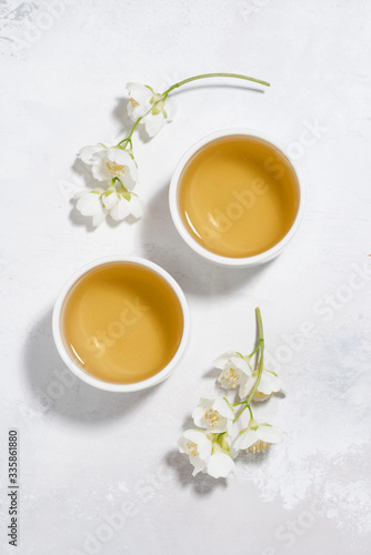 two bowls with green tea on a white background and jasmine, vertical