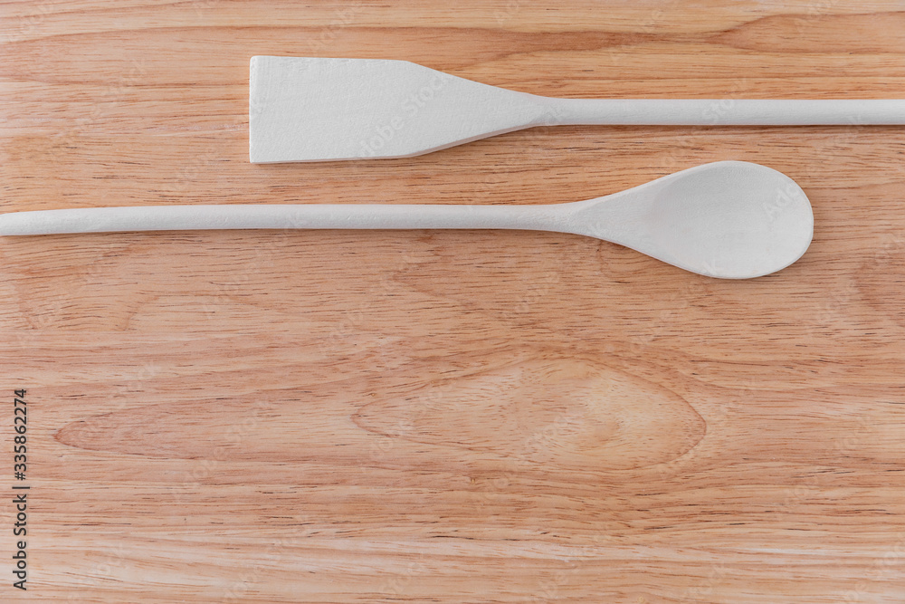 White wooden spoon and spatula lie next to each other on a light brown wooden board with stains. Amazing background for a cafe or restaurant menu, signboard.