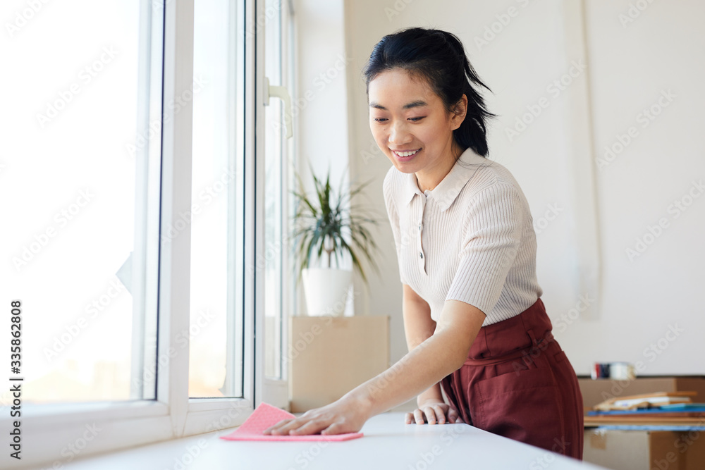 Waist up portrait of young Asian woman wiping windowsill while enjoying Spring cleaning in house or apartment, copy space Waist up portrait of young Asian woman wiping windowsill while enjoying Spring cleaning in house or apartment, copy space