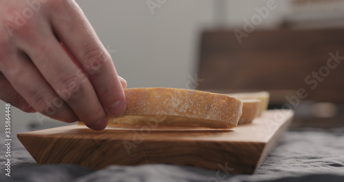man hand put ciabatta slices on olive wood board closeup