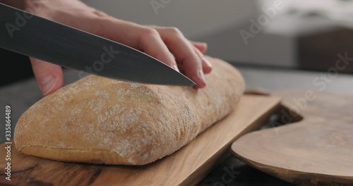 man slicing ciabatta with bread knife on olive board