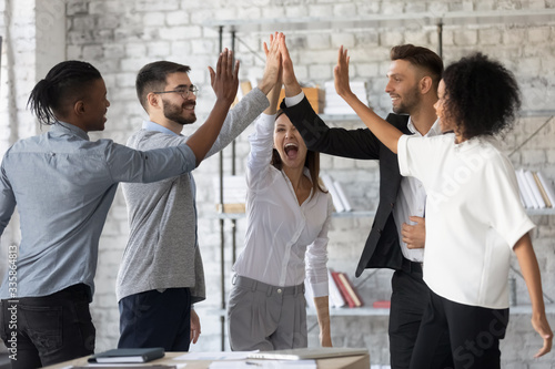 Excited successful multiracial business people giving high five, celebrating win. Good teamwork result concept. Happy employees team engaged in team building activity at corporate meeting. photo