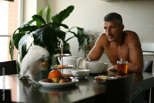 фотографія A man is having breakfast with a white cockatoo. Parrot pet