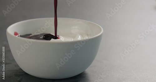 pour bilberry juice into white yogurt in white bowl on concrete surface